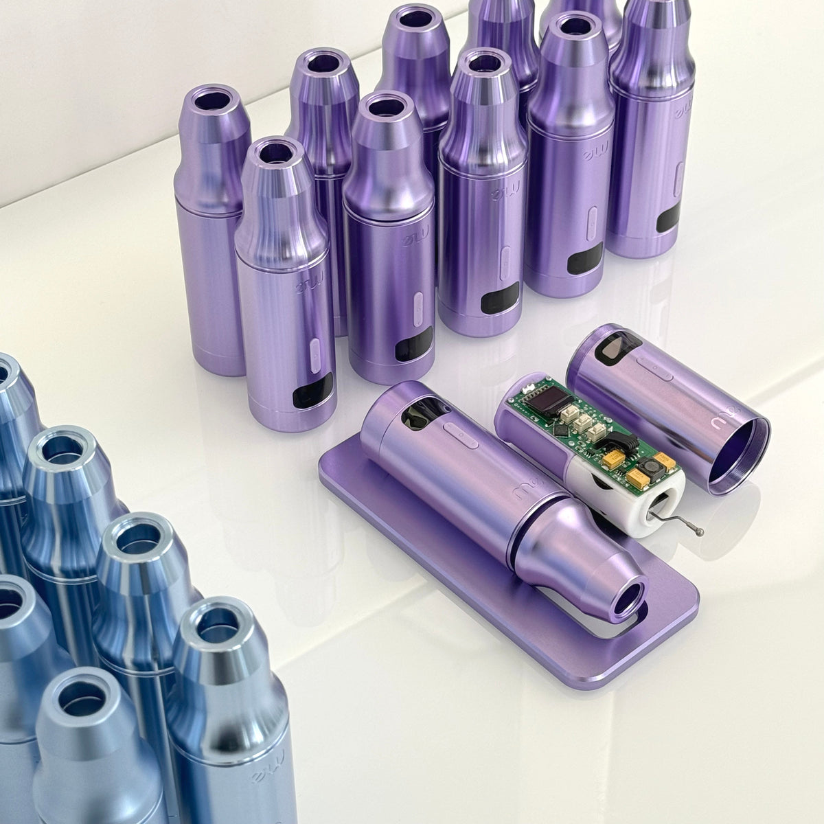 Purple and blue permanent makeup machine housings arranged on a white surface, with one machine open to show the electronics inside.